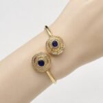 Natural oval blue sapphire and double diamond halo open cuff bangle bracelet in gold plated silver displayed on a model wrist